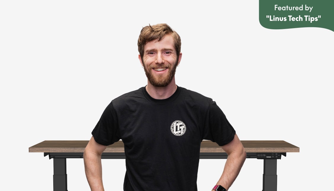 Adjustable standing desk with a dark wood tabletop and black frame, featured by Linus Tech Tips, highlighting ergonomic design and digital controls.