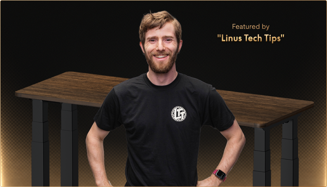 Adjustable standing desk with a dark wood tabletop and black frame, featured by Linus Tech Tips, highlighting ergonomic design and digital controls.