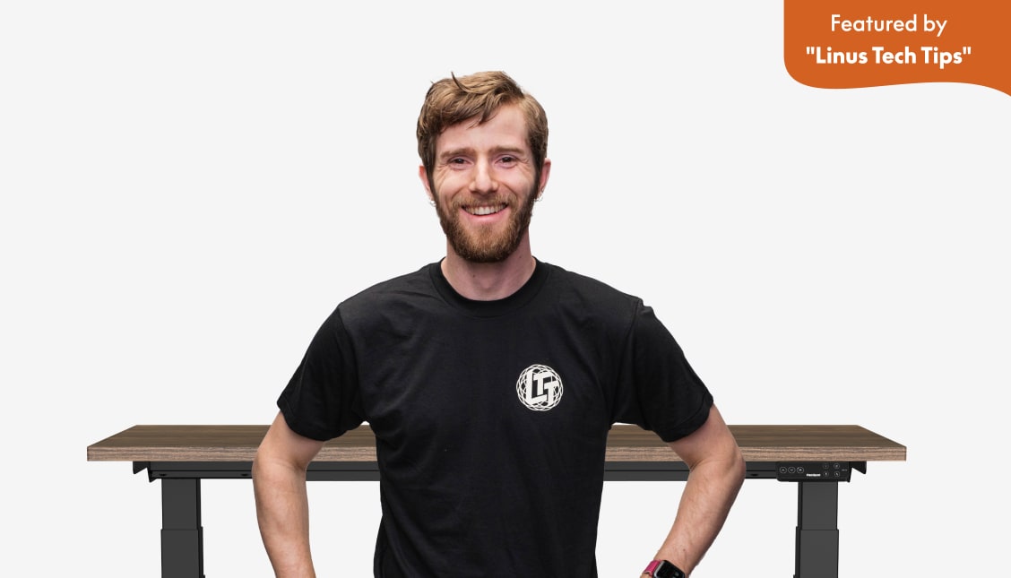 Adjustable standing desk with a dark wood tabletop and black frame, featured by Linus Tech Tips, highlighting ergonomic design and digital controls.